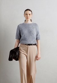 Kék kötött, rövidujjú pulóver, textúrált felülettel, beige, magas derekú nadrággal és fekete kézitáskával párosítva.