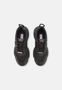 Baskets en mesh noir et cuir avec semelles épaisses, devant à lacets, languettes à l'arrière et accents de logo dorés sur la languette et les lacets.