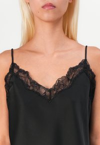 Black silk camisole featuring a deep V-neckline adorned with intricate black lace trim, thin adjustable straps, and a smooth texture.