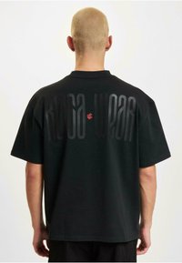 Black oversized t-shirt made of cotton, featuring large tonal "ROCA WEAR" lettering on the back in varying shades of black and red accents.