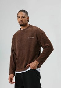 Bruine, zachte, lange mouwen sweatshirt met een gestructureerd oppervlak en een ronde hals, met een wit geborduurd logo op de borst.