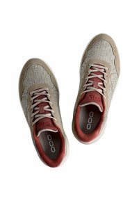 Ein Paar beige und rote Schnürsneaker mit texturiertem Obermaterial und weißen Sohlen, von oben auf einem weißen Hintergrund betrachtet.