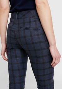 Marinblå rutiga byxor med texturerat tyg, slim fit och detaljerad bakficka, med svarta och gråa rutmönster.