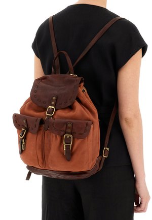 Zaino in pelle marrone con due tasche frontali, spallacci regolabili e un coperchio superiore arrotondato. Presenta dettagli di cucitura e hardware in ottone.
