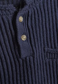Cardigan a coste blu navy con patta a bottoni e una piccola tasca sul petto. Morbida texture in maglia con dettagli di cucitura visibili.