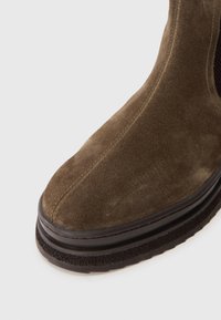 Brown suede ankle boot with a rounded toe, textured upper, and a thick, dark rubber sole featuring a patterned tread.