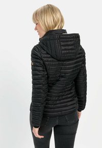Sort isoleret jakke med hætte, med quiltet tekstur og tætsiddende design. Inkluderer et logo mærke påærmet.