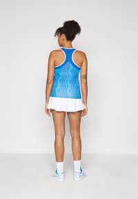 Kék sportfelső, jacquard mintával, fehér díszítéssel, és fehér szoknyával. Az öltözet hátul versenyhátú kialakítással és légáteresztő anyaggal rendelkezik.