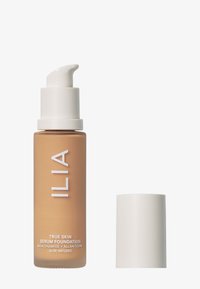 ILIA True Skin Serum Foundation i en gjennomsiktig brun flaske med en hvit pumpe, merket med produktdetaljer i hvit tekst. Kappen vises ved siden av.