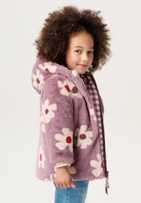 Fleecejack met lavendelkleurige achtergrond, witte bloemenpatronen en rode bloemenmiddens. Voorzien van een capuchon en een ritssluiting aan de voorkant. Gevoerd met een ruitpatroon.
