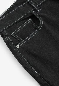 Mustat farkut, joissa on klassinen viiden taskun muotoilu, valkoiset kontrastitikkaukset ja hopeinen metallinen nupukka etutaskussa.