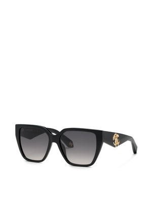 Lunettes de soleil noires de style œil de chat avec des verres dégradés foncés et un emblème décoratif doré sur la branche, présentées sur fond blanc.