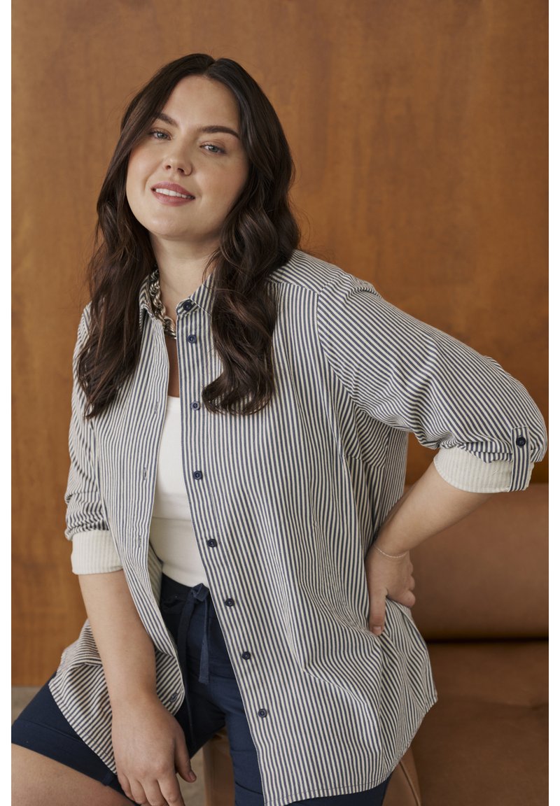 Chemise à rayures bleu marine et blanc, boutonnée, avec une coupe décontractée, manches longues retroussées et tissu contrastant aux poignets.