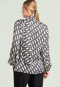 Langærmet bluse i creme og marineblå med et bølgemønster, med høj krave og løstsiddende pasform, lavet af letvægtsstof.