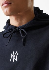 Sudadera negra de tela suave con un logo bordado en blanco en el pecho, y con un cordón ajustable en el cuello.