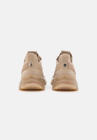 Chaussures de sport beiges avec dessus en maille texturée, col rembourré et semelle en caoutchouc. Logo "STRIDEN" embossé à l'arrière.