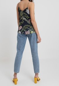 Camisole w kwiatowy wzór w kolorze granatowym z cienkimi ramiączkami, w połączeniu z jasnoniebieskimi dżinsami. Żółte sandały na słupku dopełniają strój.
