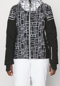 Veste à motifs noir et blanc avec fermeture éclair à l'avant, capuche et poignets élastiques. Présente des motifs géométriques sur le corps et des manches noires.