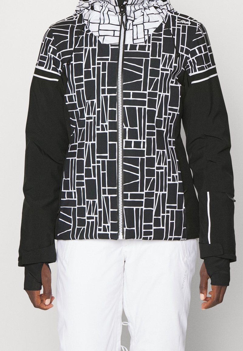 Veste à motifs noir et blanc avec fermeture éclair à l'avant, capuche et poignets élastiques. Présente des motifs géométriques sur le corps et des manches noires.