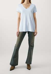 Svetle modré tričko s výstřihem do V vyrobené z měkké tkaniny, kombinované s vybledlými džíny bootcut. Oblečení má volný střih a minimální detaily.