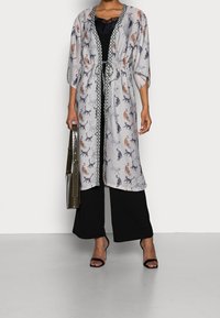 Lättvikts, lång kimono i grått tyg med kattmönster i orange, svart och blått. Har ett knytliv och kontrasterande trim.