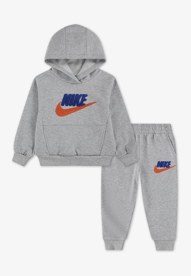 Pelēkā kapuce un sporta bikses komplekts, kas rotāts ar izšūtu zilo "NIKE" tekstu un oranžo svītru logo. Mīksta auduma ar ribotām piedurknēm un jostu.