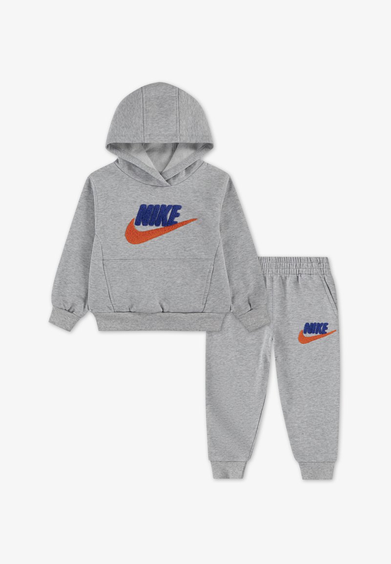 Siva kapuca in hlače z žico, ki prikazuje vezeno modro besedilo "NIKE" in oranžno ikono. Mehka tkanina z rebrastimi manšetami in pasom.