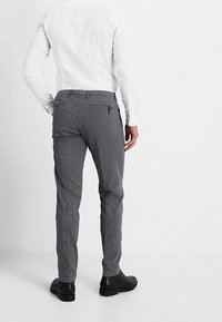 Šedé vzorované kalhoty s úzkým střihem, s knoflíkovou kapsou na zadní straně a jemnou texturou. Kombinovány s černými botami.