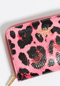 Roze portemonnee met zwarte luipaardvlekken, glanzende textuur, ritsluiting en gouden branding "Bimba y Lola" aan de voorkant.