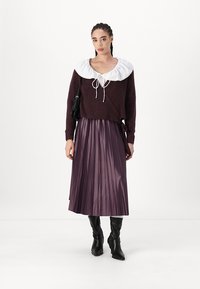 Maglione borgogna a trama con colletto bianco a ruches e dettagli con fiocco; abbinato a una gonna a pieghe color malva e stivali neri al ginocchio.