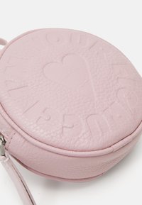 Borsa a tracolla rotonda in pelle rosa con testo in rilievo e design a cuore, caratterizzata da una texture liscia e una tracolla sottile regolabile.