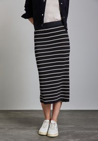 Gonna a matita in maglia con righe orizzontali nere e crema, caratterizzata da una vita alta. Abbinata a sneakers bianche e a un top neutro.