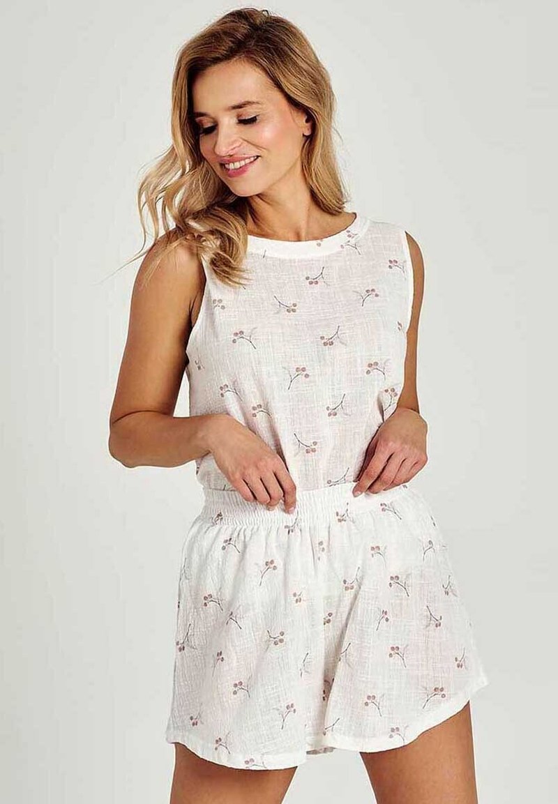 Letni kombinezon bez rękawów w białym materiale z kwiatowym wzorem, elastycznym paskiem w talii oraz delikatnymi różowymi i zielonymi akcentami.