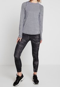 Koszula w paski z długim rękawem w kolorze granatowym i białym, połączona z czarnymi legginsami w wzory, charakteryzująca się dopasowanym fasonem i teksturowaną tkaniną. Czarne sneakersy.