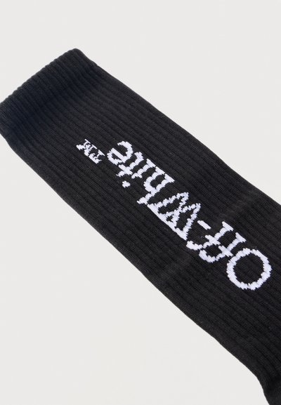 Manche en tissu côtelé noir avec le texte blanc "Off-White" tricoté en diagonale au centre sur un fond clair uni.