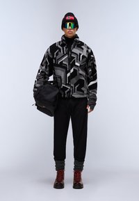 Giacca in pile a fantasia nera e grigia, dolcevita nero, pantaloni neri larghi, accenti in lana ai polsi, stivali rossi con lacci, mentre porta una borsa nera.