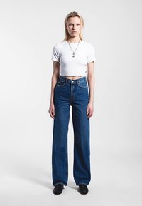 White cropped t-shirt paired with high-waisted, wide-leg dark blue jeans. Plain design with a silver necklace and black shoes.