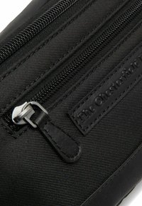 Zwarte nylon tas met dubbele ritsen, getextureerd oppervlak en een leren patch met "The Chesterfield Brand" in reliëf.