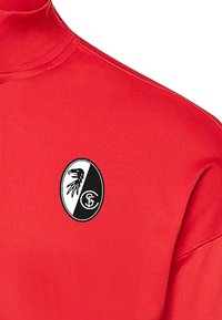 Rode langarmshirt met een zwart-witte ronde logo met een vogeldesign. Het materiaal lijkt glad en heeft een aansluitende kraag.