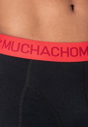 Czarne majtki z szerokim, czerwonym elastycznym paskiem w talii, na którym wyraźnie widnieje napis "MUCHACHO". Gładka faktura z widocznymi detalami szwów.