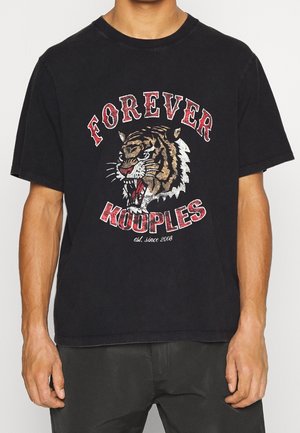 Osoba w czarnej koszulce z grafiką ryczącego tygrysa i czerwonym napisem "FOREVER KOUPLES est. since 2008" z przodu.
