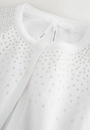 Cardigan alb cu detalii din mărgele argintii, închidere cu nasturi și textură moale. Are un mic fundiță la gât, iar eticheta indică brandul și originea.