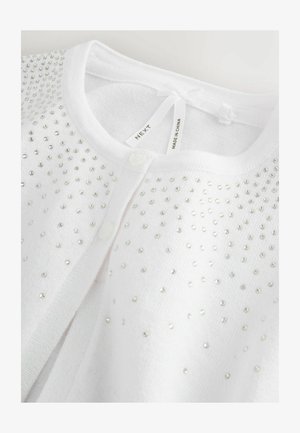 Biały kardigan z detalem z srebrnych koralików, zapięciem na guziki i miękką teksturą. Na szyi znajduje się mała kokardka, metka wskazuje markę i pochodzenie.