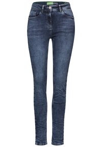 Jeans ajustados en denim azul oscuro con una textura suave, diseño de cinco bolsillos, cremallera y etiqueta verde contrastante en la cintura.