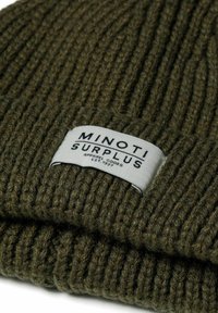 Rebrasti, maslinasto zeleni pleteni zimski šešir s preklopom i pravokutnom etiketom s crnim natpisom "MINOTI SURPLUS."
