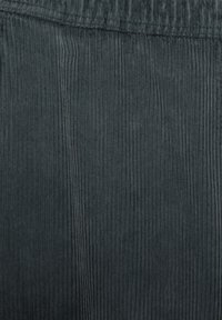 Tmavohnedá jemná kordová tkanina s úzkymi vertikálnymi rebrami a mäkkou textúrou; na vrchu má elastický pás.