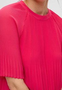 Top plisado rosa con un escote redondo, textura suave y mangas sueltas tipo volantes, que presenta líneas verticales paralelas en una tela ligera.