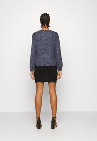 Blusa blu navy con pois bianchi, maniche lunghe a sbuffo e scollatura rotonda, abbinata a una mini gonna nera aderente e scarpe con tacco nere.