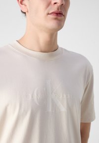 Light beige cotton t-shirt featuring a round neck, short sleeves, and a subtle embossed logo: "Calvin Klein Jeans" with a large "CK."