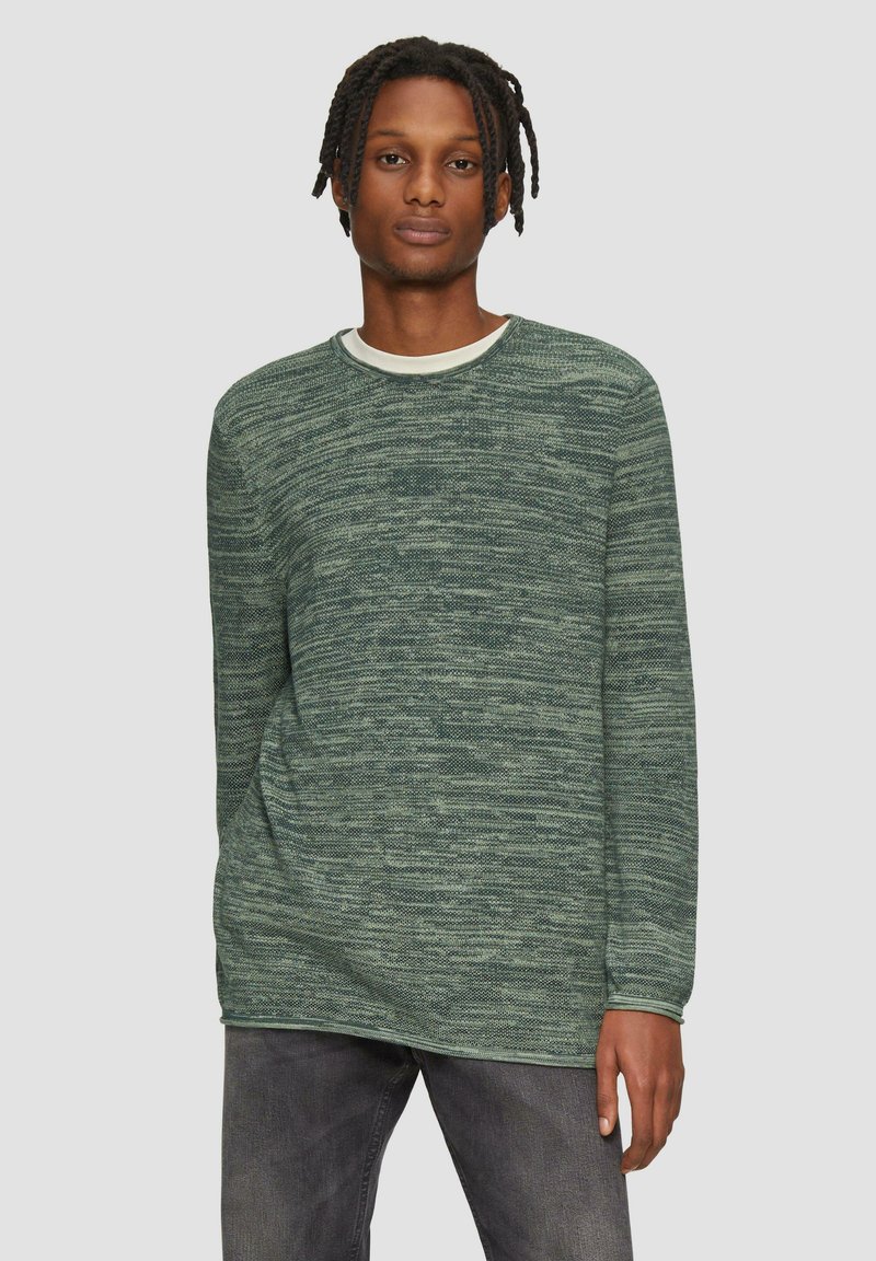 Groene gestructureerde trui met lange mouwen en een ronde hals, met een contrasterende binnenkraag, gecombineerd met grijze jeans.